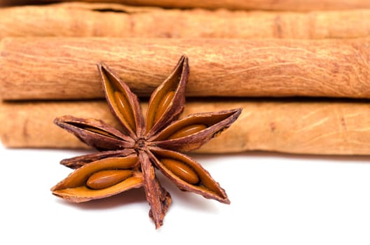 Star anise in front of cinnamon sticks on white background