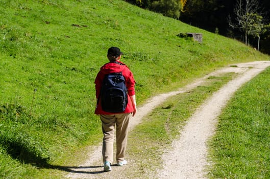 Woman in red jacket and backpack while hiking on a green meadow