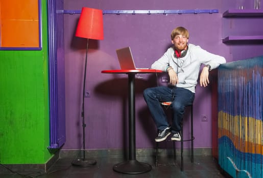Young man sitting working on laptop in colourful location