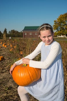 young girl holding pumkin on knee in field