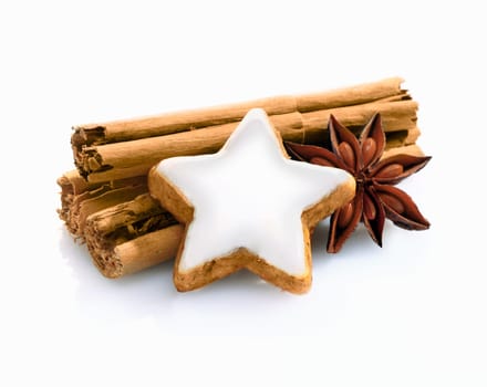 Christmas spice still life with cinnamon stiicks and star anise and a decorative star shaped iced biscuit on a white background