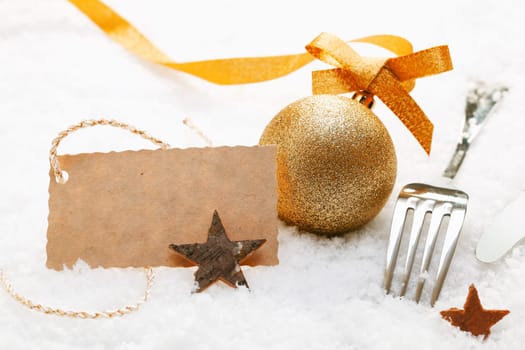 Festive place setting with Christmas decorations and silver cutlery in fresh winter snow with a decorative blank gift tag
