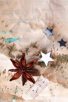Grungy Christmas background with crumpled old paper scattered with stars , a star anise spice and part of a music score with copyspace