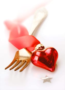 Romantic red heart decoration with twirled ribbon lying across a fork in a Christmas, Valentines, wedding or anniversary background