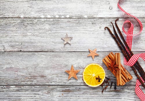 Colourful array of decorative Christmas spices with a fresh red and white checked twirled ribbon on a background of grungy textured weathered white wood