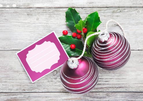 Christmas tag background with colourful spiral patterned purple baubles and holly on white painted wooden boards