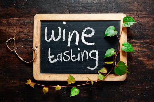 Handwritten decorative Wine tasting sign on a small rustic slate chalkboard with trailing leaves from a green creeper and dark textured wood background