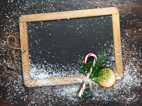 Blank rustic Christmas chalkboard slate with scattered snow and a colourful striped candy cane ready for your seasonal greetings