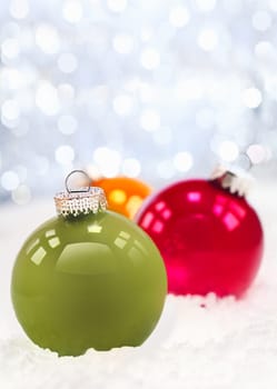 Winter snow and pretty green and red Christmas baubles agaisnt a sparkling bokeh of party lights with copyspace