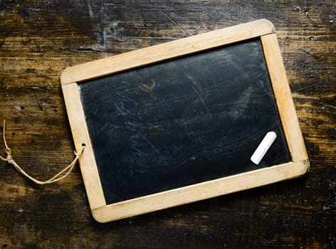 Smal wooden framed blank blackboard with a piece chalk on a darl timber background with woodgrain suitable for your greeting, message or menu