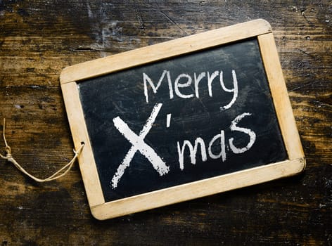 Merry Xmas greeting handwritten on a small slate chalkboard lying on old textured wooden boards