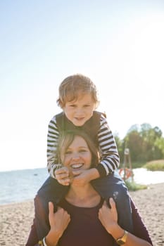 Mother carrying son on shoulders and having fun together at the beach.