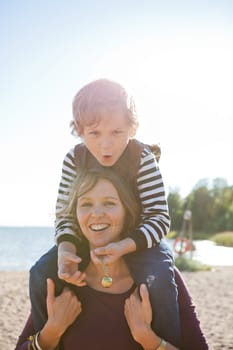 Mother carrying son on shoulders and having fun together at the beach.