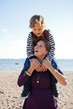 Mother carrying son on shoulders and having fun together at the beach.
