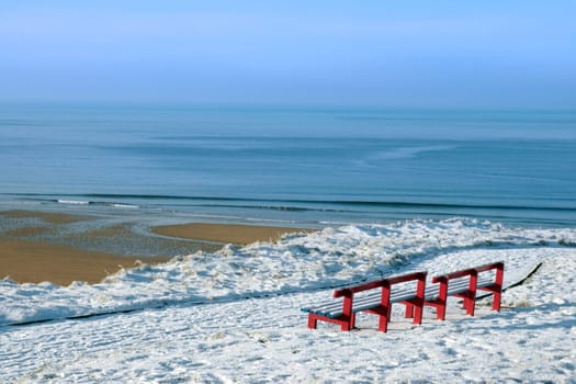 a seasonal snow covered view of atlantic ocean and ballybunion beach with red benches on a frosty snow covered winters day