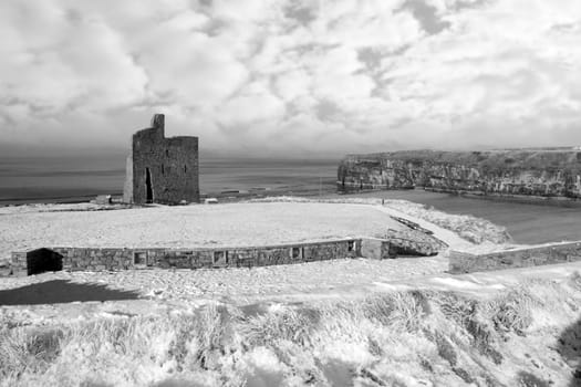 a seasonal snow covered view of atlantic ocean and ballybunion castle beach and cliffs on a frosty snow covered winters day in black and white