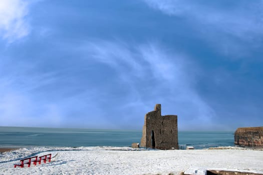 a seasonal snow covered view of atlantic ocean and ballybunion castle with red benches on a frosty snow covered winters day