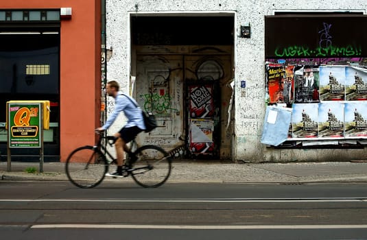A shopping street in Berlin Mitte,a cyclist passes a house entrance with graffiti and posters.