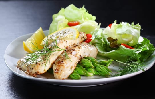 Delicious fried fish on green asparagus with salad