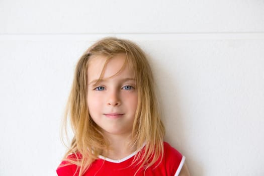 Blond beautiful kid girl smiling on a white wall portrait