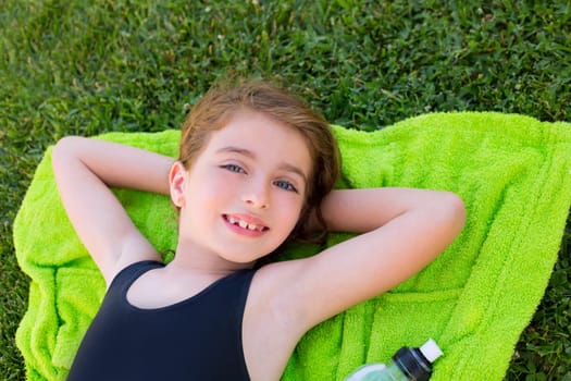 children girl relaxed lying on towel over green grass with water bottle in swimsuit