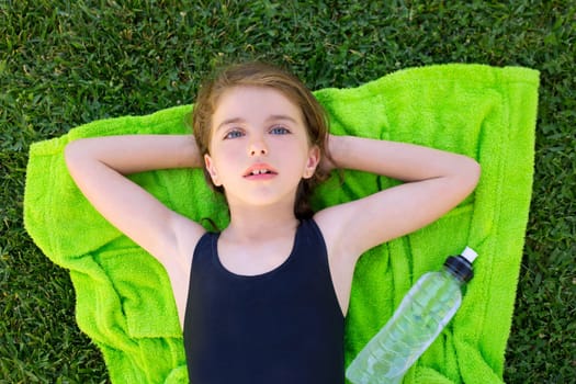 children girl relaxed lying on towel over green grass with water bottle in swimsuit