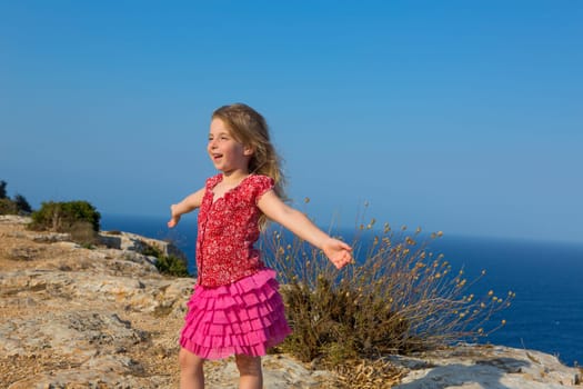 blue day with kid girl open hands to the wind and Mediterranean sea