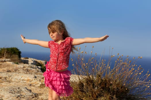blue day with kid girl open hands to the wind and Mediterranean sea