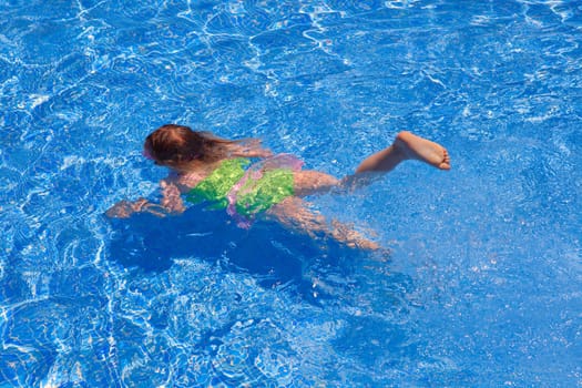 children gilr swimming underwater in blue tiles pool