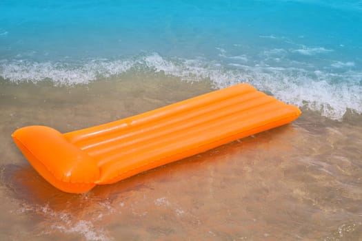 Beach shore with orange floating lounge and waves over sand bottom