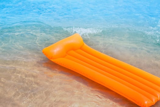 Beach shore with orange floating lounge and waves over sand bottom