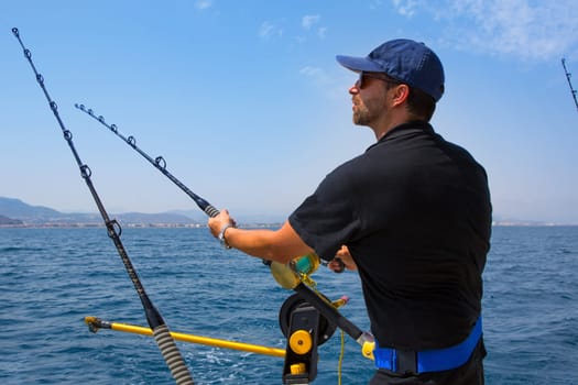 blue sea fisherman in trolling boat in action with downrigger and rod