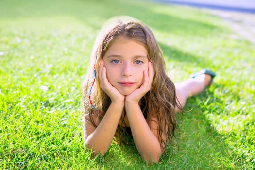 blue eyes children girl relaxed on the garden grass lying with hands in face