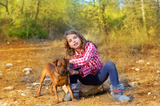 children girl sitting in the pine forest holding little dog mini pinscher