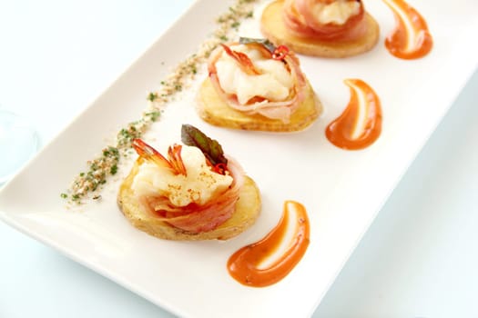 Delicious and delicate shrimps wrapped in bacon on potato slices with a spinach leaf.