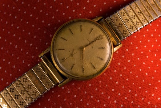 Retro golden wristwatch close up on red vintage cloth background.