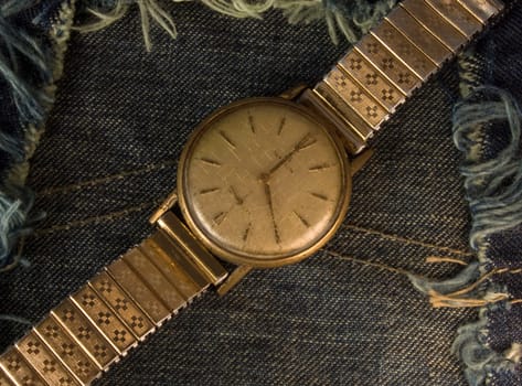 Retro golden wristwatch close up over blue jean cloth background.