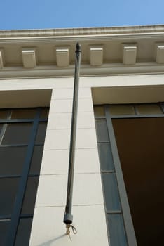 Architectural detail of an antique building with a flagpole. Blue sky background. Bottom View