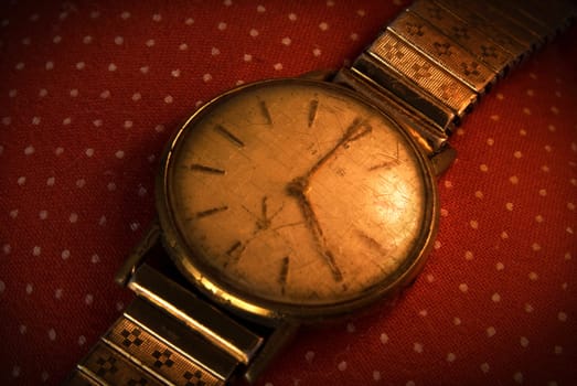 Retro golden wristwatch close up on red vintage cloth background.