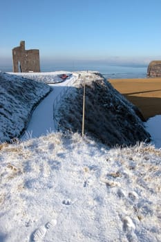 a seasonal snow covered view of atlantic ocean and ballybunion castle beach and cliffs on a frosty snow covered winters day