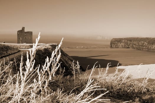 a seasonal snow covered view of atlantic ocean and ballybunion castle beach and cliffs on a frosty snow covered winters day in sepia