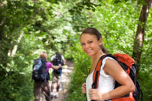 group of man and women during hiking excursion in woods, with woman looking at camera and smiling. Waist up