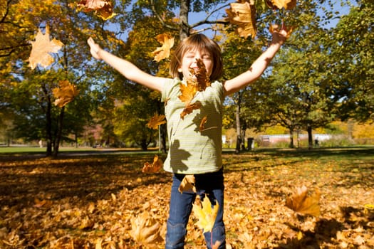 Girl throws colorful leaves in autumn and is happy