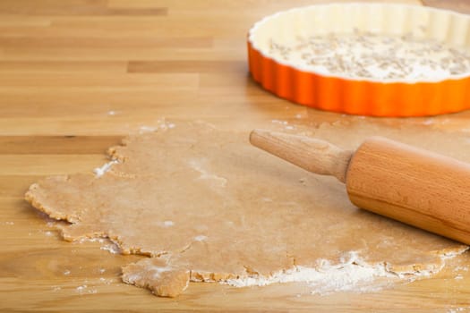Dough for a quiche on wooden table in the background with quiche shape