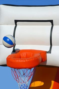 Ball getting into the basket. Partial view of a colorful inflatable basketball toy on blue sky background