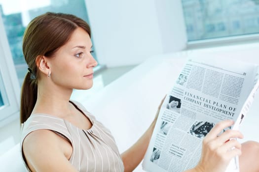 Attractive business lady with a newspaper being absorbed in her thoughts