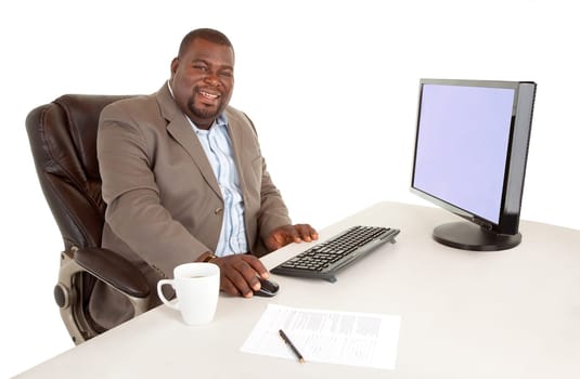 An African American businessman is sitting at his desk while smiling at the camera.