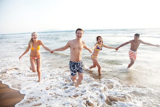 group of young people having fun, running in the surf