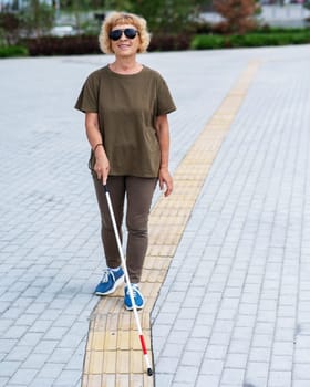 An elderly blind woman walks with a cane along a tactile tile