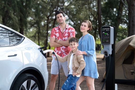 Outdoor adventure and family vacation camping in nature travel by eco friendly car for sustainable future. Lovely family recharge EV car with EV charging station in campsite. Perpetual